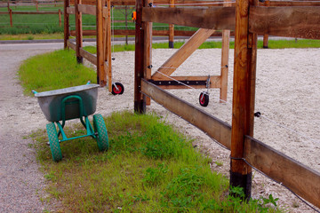 The empty stable. Empty open paddock for horse riding. Wheelbarrow for manure near an empty stable. Stable, cleaning concept.