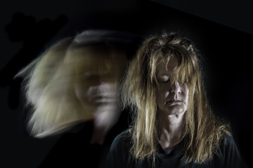 Portrait of a red-haired middle-aged woman in front of black background. Beside her are ghostly...