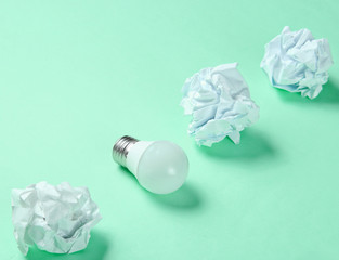 Energy saving light bulb and crumpled paper balls on green background. Minimalistic business concept, idea.