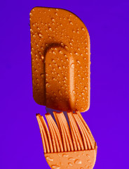 Silicone kitchen brush and spatula for cooking in drops of water on purple background