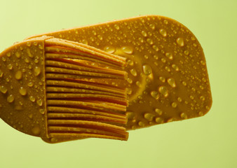Silicone kitchen brush and spatula for cooking in drops of water on yellow background