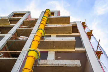 Suspended sections of yellow garbage chute on a facade of building under construction against blue...