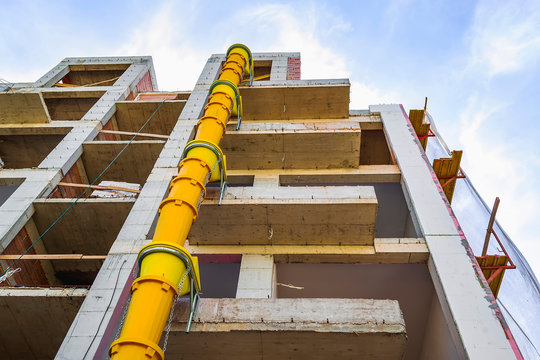 Suspended sections of yellow garbage chute on a facade of building under construction against blue sky with white cloud.