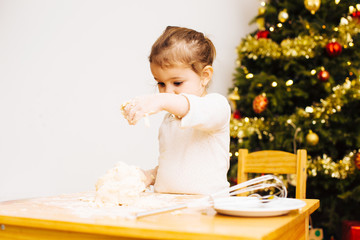 Little girl sprinkling flour on dough next to christmas tree
