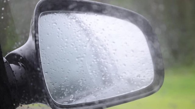 Car Side Mirror And Drivers Window With Drops Of Rain Sliding Down It.