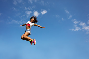 Happy young school age girl jump high over sky