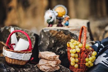 Grape, apple, banana, candles and gifts served at a picnic on the stone. Basalt. picnic laid out on a rock with a wicker basket  and fresh grapes. Tasty spring picnic on a rock. Two figures of trolls