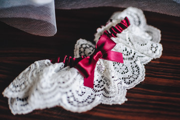 Fototapeta na wymiar white wedding garter with a red bow on a brown table