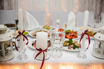 On the table are white wedding candles with red bows. Meals. Food. Family candle. Wedding candles..Lights. The bright light. Glow lights. flowers. Candles.