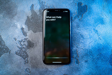 Phone on concrete surface and activated by voice digital assistant, text on smartphone screen: What...