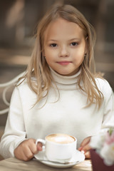 Pretty little girl smiling and drinking cappuccino in outdoor cafe