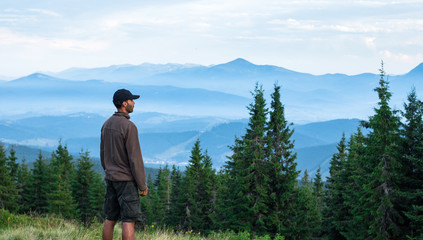 hiker man in cap admires the scenery of mountain range covered with blue fog in carpathian mountains
