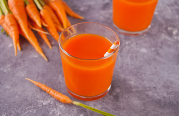 Carrot juice in glasses and young carrots on concrete background