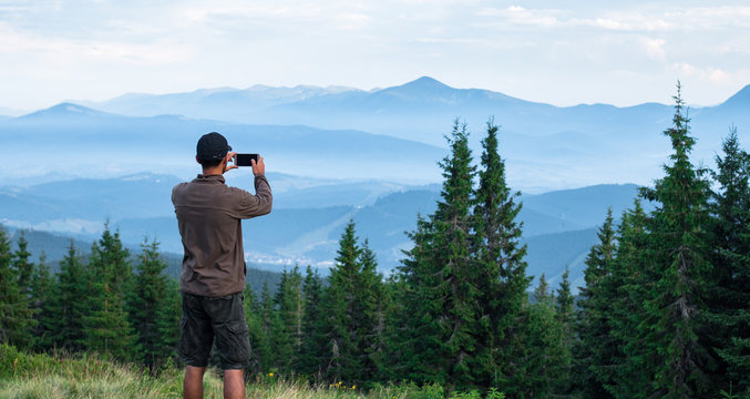 hiker man in cap taking photos of mountain range covered with blue fog in carpathian mountains