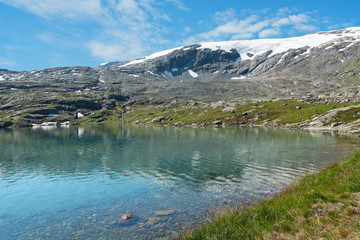 Naklejka na ściany i meble Blue lake landscape with snow covered mountain, Norway. Nibbevegen road to Dalsnibba mountain from Geiranger.