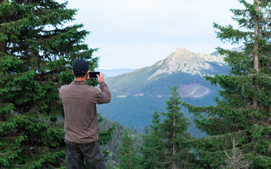 Fototapeta na wymiar hiker man in cap taking photos of mountain range in the carpathian mountains gorgany