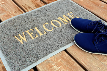 Welcome is written on the rug and shoes are standing nearby
