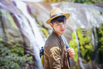 Male tourists wearing a hat against a beautiful waterfall background, handsome man with nature tourism