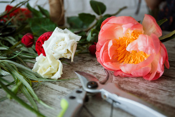 Secateurs on a wooden background next to greens and flowers. Concepts of floristry, bouquet assembly, floristry, handmade details