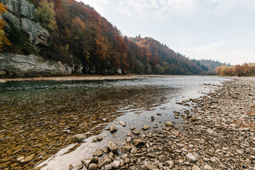 Fototapeta premium Clear river with rocks leads towards mountains..lit by sunset. Mountain fast flowing river stream of water in the rocks with blue sky. Landscape with forest, river and stones. The mountain river.