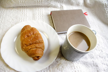 .breakfast with coffee and croissants, on a light background with a notebook