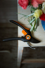 Secateurs on a wooden background next to greens and flowers. Concepts of floristry, bouquet assembly, floristry, handmade details