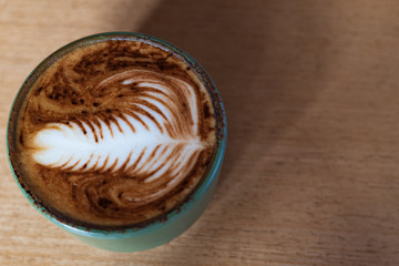 Cappuccino coffee with latte art milky foam on wooden table background.
