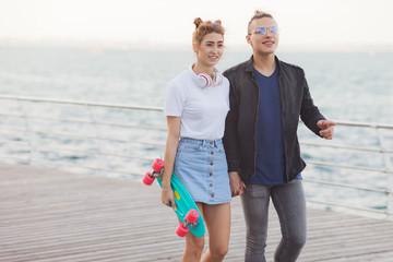 Youth summer time. Stylish hipster couple in love strolling along the beach promenade.