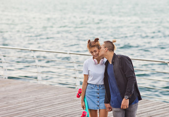 Youth summer time. Stylish hipster couple in love strolling and kissing along the beach promenade.