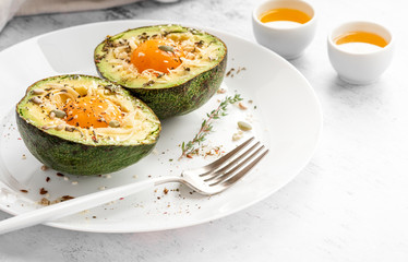 Tasty and healthy avocado snack. Slices of avocado with raw yolk, cheese, olive oil and spices on a white plate close-up.