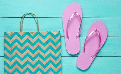 New pink flip flops and paper bag on blue wooden background. Shopping concept. Top view