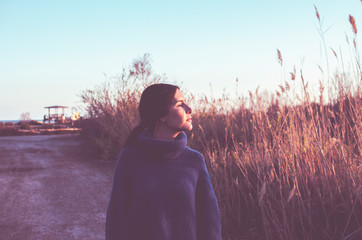 young woman with pigtail wears sweater at sunset in the countryside