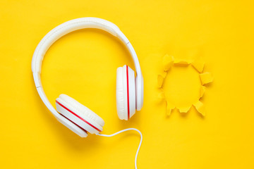 Classic white wired headphones on purple yellow paper background with torn hole. Retro style. 80s. Pop culture. Top view. Minimal Music Concept