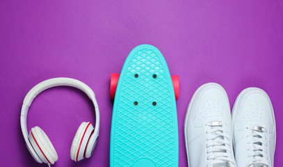 Hipster outfit. Skateboard with headphones and sneakers on purple background. Creative fashion minimalism. Trendy old fashionable style. Minimal summer fun. Music concept