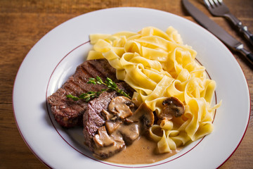 Grilled beef steaks and noodles in creamy mushroom sauce, garnished with thyme on white plate