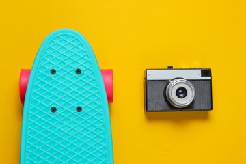 Retro set with blue skateboard and retro camera on yellow background. Studio shot. Youth lifestyle. Top view