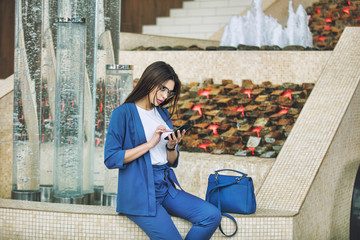Young adult beautiful brunette girl happy on the background of fountains in the business center with a mobile phone in her hands