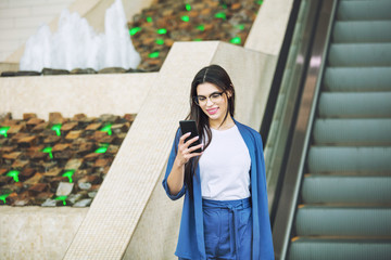Young adult beautiful brunette girl happy on escalator with mobile phone in hands