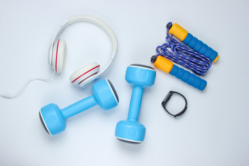 Dumbbells, smart bracelet, headphones,  jump rope on a white background. Minimalistic sport concept. Top view.