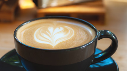 Latte art coffee in black cup set on wooden table, beverage art by fresh milk with coffee.