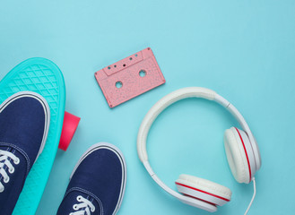 Hipster outfit. Skateboard with headphones, audio cassette and sneakers on blue background. Creative fashion minimalism. Minimal summer fun. Pop art. 80s. Top view