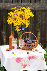 bouquet of flowers, wine, glasses and grapes against the background of an old fence
