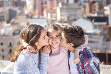 Dos hermanos besando a la vez a su hermana pequeña en la azotea