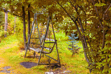 An old retro iron wrought metal swing with a wooden bench in a vintage style stands in a garden or...