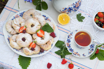 Still life with bouquet of flowers, tea, cookies and berries on table in garden