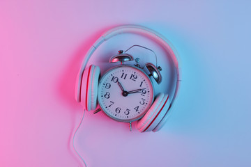 Creative music concept. Retro alarm clock and classic headphones with gradient pink-blue neon light. Pop culture. 80s. Top view