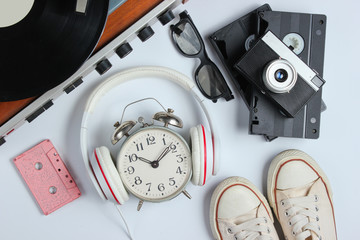 Flat lay retro 80s pop culture objects. Vinyl player, headphones, audio cassette, video tapes, alarm clock, film camera, sneakers on white background. Top view