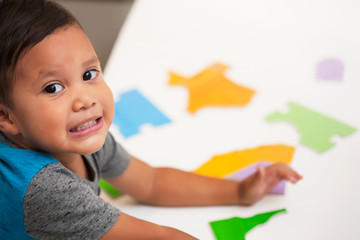 A preschool age young boy  having fun and smiling while playing with manipulative toys on a white table.