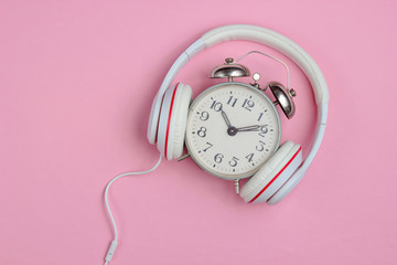 Creative music concept. Retro alarm clock and classic headphones on pink background. Pop culture. 80s. Top view