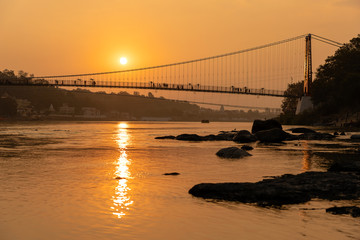Obraz premium Beautiful view of Ganges river embankment and bridge at sunset. Rishikesh, India